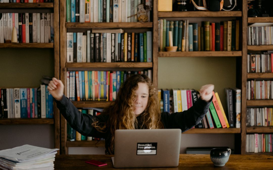 Girl at computer at home with arms raised