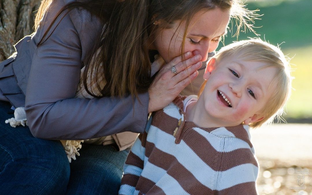 Mom speaking into boy's ear and he is smiling